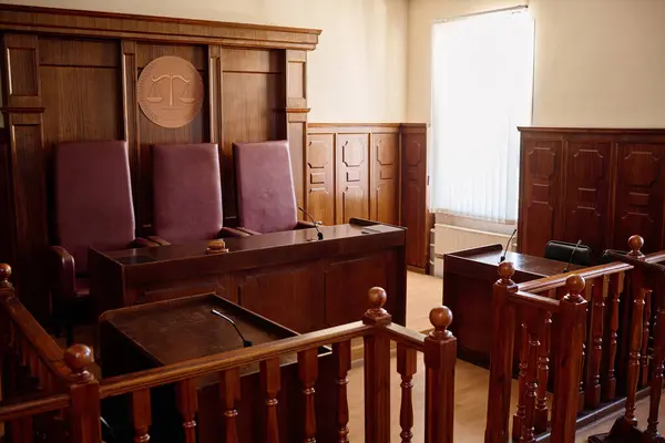 Part of spacious courtroom with wooden furniture and leather chairs for judges standing by their desk with microphone and gavel