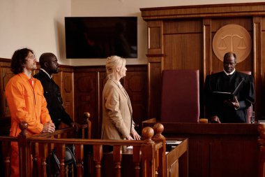 Olgun kadın avukat, polis ve genç erkek şüpheli siyah manto giyen tarafsız bir yargıca bakıyor.