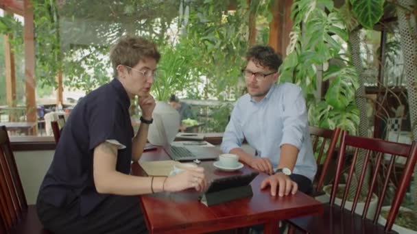 デジタルタブレットでビジネスプランを議論しながら 夏の日に屋外カフェでコーヒー休憩で会う若者と女性のショットでズーム — ストック動画