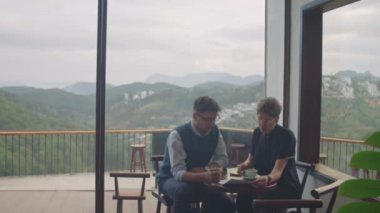 Kafede oturan erkek ve kadın meslektaşların geniş açılı fotoğrafları. Pahalı dağ manzaralı ve kahve içerken iş kağıtlarını tartışıyorlar.