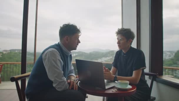 男性和女性同事坐在山景咖啡店的笔记本电脑和咖啡旁边 一边工作一边讨论项目 — 图库视频影像