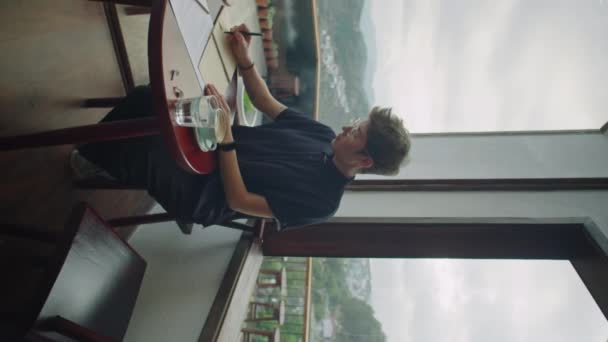 坐在山景咖啡馆餐桌旁的年轻女子的垂直全照 并在抄本上记笔记 — 图库视频影像