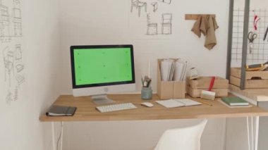 Ahşap atölyesinde yeşil ekranlı ve kablosuz klavyeli bilgisayarın duvarında sandalye inşa planları, araçlar ve çalışma yeriyle ilgili dosyalar olan ark görüntüsü.
