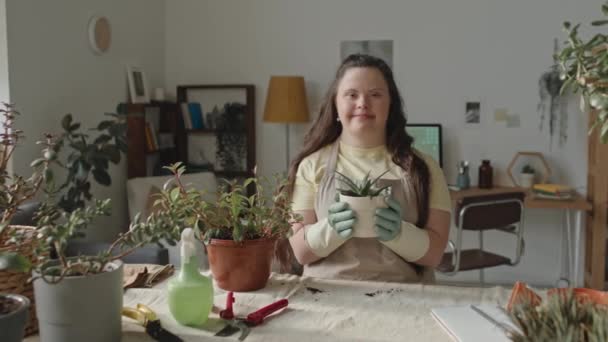 Portret Wesołej Dziewczyny Zespołem Downa Fartuchu Rękawiczkach Trzymających Doniczkową Roślinę — Wideo stockowe