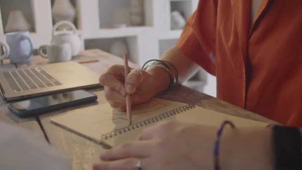 陶芸のワークショップでデスクで働いている間 鉛筆でコピーブックでスケッチを描く女性アーティストのショット — ストック動画