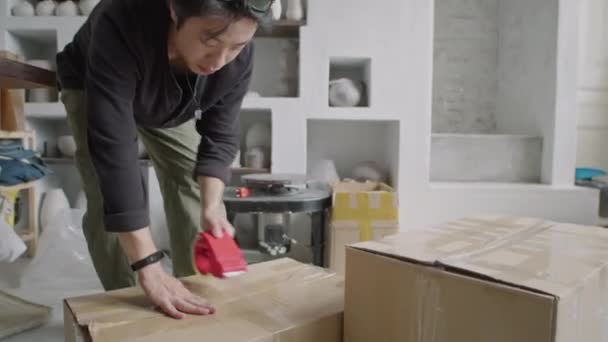 Jonge Aziatische Keramist Verzegeling Kartonnen Doos Met Plakband Tijdens Voorbereiding — Stockvideo