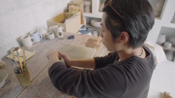 工作室工作场所小瓷轮上年轻亚洲雕塑家粘土的高角镜头拍摄 — 图库视频影像