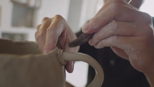 陶芸スタジオで働いている間ポッターの肋骨が付いている粘土のマグにハンドルを付ける専門の男性の陶芸家のクローズアップ ショット — ストック動画