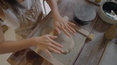 Seramik ana sınıfında çömlek yaptığı için önlüklü, yuvarlanan killi bir kadın resmi.