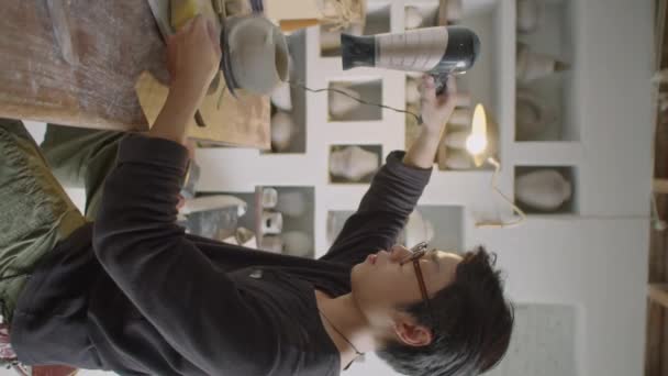 Vertikale Aufnahme Eines Jungen Asiatischen Keramikers Mit Haartrockner Beim Trocknen — Stockvideo