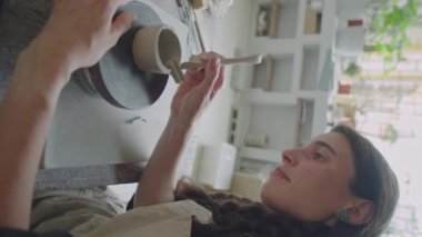 Ana zanaat sınıfında seramik öğrenirken çömlek çarkında kupa şekillendiren kızın dikey görüntüsü.