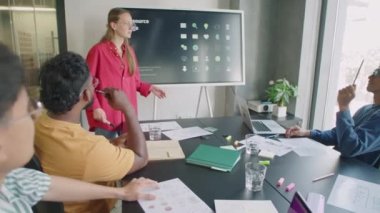Genç iş kadını, ofiste yapılan takım toplantısında çok ırklı erkek arkadaşlara dijital ekranda sunum yapıyor