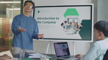 Orta yaşlı Asyalı işadamı, ofis toplantısı sırasında dijital ekranda sunum yapıyor ve şirket misyonunu meslektaşlarına anlatıyor