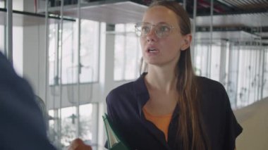 Elinde dosya olan genç bir iş kadınının omzundan vurularak ikinci kattaki korkulukların yanında dururken iş arkadaşıyla konuşması...