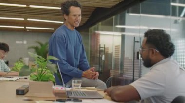İki çok ırklı adam ortak çalışma odasında oturup ofiste çalışırken iş hakkında sohbet ediyorlar.