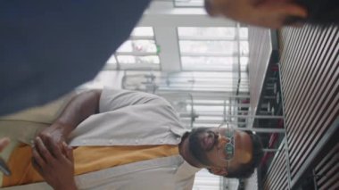 İş merkezinde korkulukların yanında yan yana dururken Hintli bir adamın iş arkadaşıyla tartışırken çekilmiş dikey bir fotoğrafı.