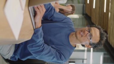 Asyalı bir adamın günlük kıyafetleri ve gözlükleriyle ofisteki laptopta çalışırken dikey görüntüsü.