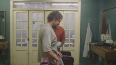 Afro-Amerikalı erkek berber müşteriyi yumruk tokuşturarak selamlıyor ve berber dükkanında saçını kesmeden önce ona kuaförlük pelerini giydiriyor.