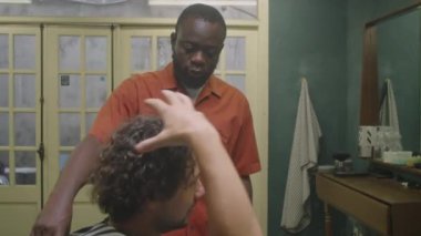 Afrika kökenli Amerikalı berber erkek kıvırcık saçlı müşteriyle saç kesimini tartışıyor.