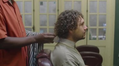 Profesyonel Afro-Amerikan berber, erkek müşterisinin saçını kesmeye hazırlanırken boynuna bant ve pelerin takıyor.