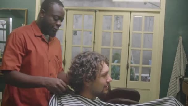 Afroamerikanischer Friseur Setzt Männlichen Kunden Gestreiftes Friseurumhang Auf Und Plaudert — Stockvideo