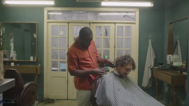 Середній Довгий Знімок Чорного Перукаря Обрізає Волосся Чоловічого Клієнта Підстригачами — стокове відео