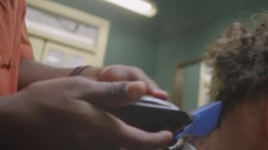 Berber dükkanında çalışırken saç makasıyla erkek müşterinin yakasını budayıp tarayan siyah berberin yakın çekim görüntüleri.