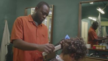 Eski moda berber dükkanında saç kesme makinesi ve tarak kullanarak erkek müşteriye saç keserken orta boy bir resim.