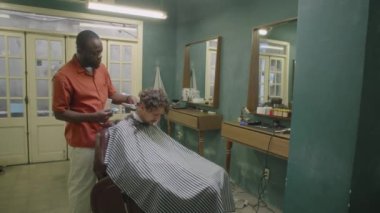 Afrika asıllı Amerikalı berberin saç makasıyla erkek müşterinin boynunu tıraş ederken ve eski moda berber dükkanını tararken.