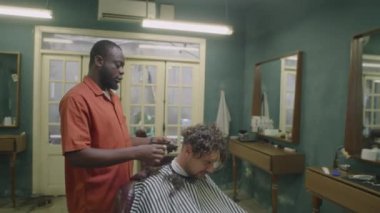 Eski moda berber dükkanında erkek müşterinin ensesini tıraş ederken, saç makasıyla ve fırçayla çalışan Afrikalı Amerikalı berberin orta boy uzun pozu.