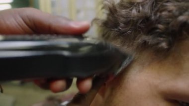 Saç kesme makinesiyle erkek müşterinin kulağının arkasındaki kılları tıraş ederken ve fırça kullanırken yakın çekim.
