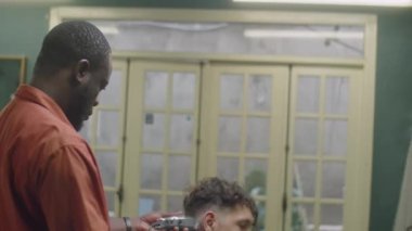 Eski moda kuaförde çalışırken erkek müşterinin yakasını bukle ve tarak ile tıraş eden Afrikalı Amerikalı berber.