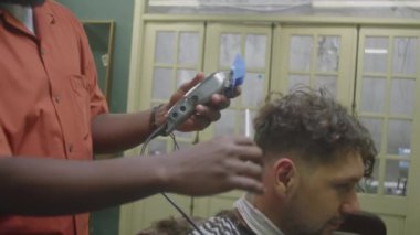 Siyah berberin saç kesme makinesiyle erkek müşterinin yakasını traş ederken ve eski moda berber dükkanında çalışırken tarağını eğik bir şekilde çek.