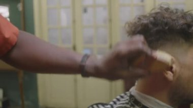 Erkek berberin saç fırçasıyla saç kesimini kestikten sonra erkek müşterisinin boynundaki kılları keserken çekilmiş bir fotoğrafı.