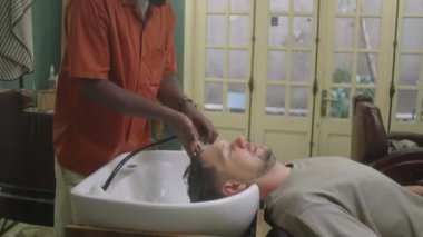 Eski moda berber dükkanında siyah berber erkek müşterinin saçını yıkıyor.