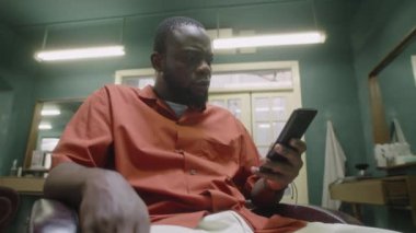 Eski moda berber dükkanında oturup cep telefonuyla konuşan siyah erkek berberin düşük açılı görüntüsü.