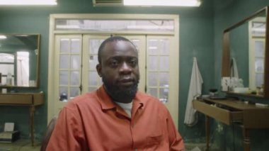 Afrika kökenli Amerikalı erkek berberin retro berber dükkanında otururken ve akıllı telefondan internette sörf yaparken çekilmiş bir fotoğrafı.