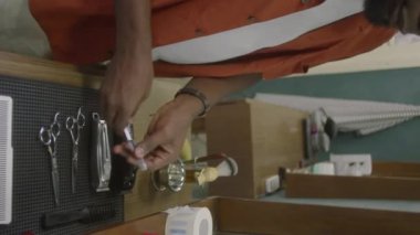 Berber dükkanında çalışmaya hazırlanırken siyah erkek berberin kuaför aletlerini masaya koyarkenki dikey kesimi.