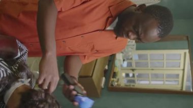 Müşteriyle kuaförde çalışırken siyah erkek berberin saç kesimi ve tarak kullanmasının dikey görüntüsü.