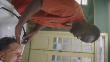 Berber dükkanında Afrikalı Amerikalı berberin duş alırken ve erkek müşterinin saçını yıkarken dikey pozu.