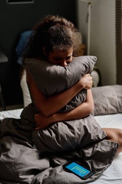 Geceleri çift kişilik yatakta akıllı telefonuyla oturup siber zorbalık mesajlarından muzdarip zavallı genç kız yastıkta ağlıyor.