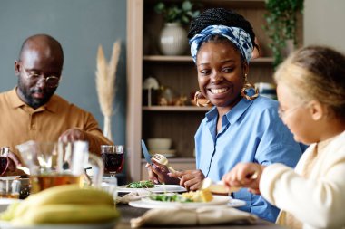 Kocasıyla tatlı kızı arasında otururken neşeli masasında kızına bakan mutlu Afrikalı genç bir Amerikalı kadına odaklan.