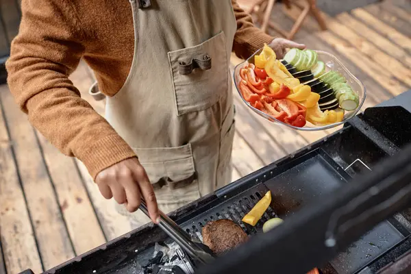 High angle view of woman frying meat and vegetables on grill at picnic outdoors