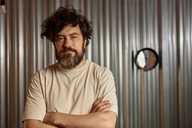 Aşırı büyümüş saç stili sakallı bir adamın portresi. Berber dükkanında kollarını kavuşturmuş kameraya bakıyor.