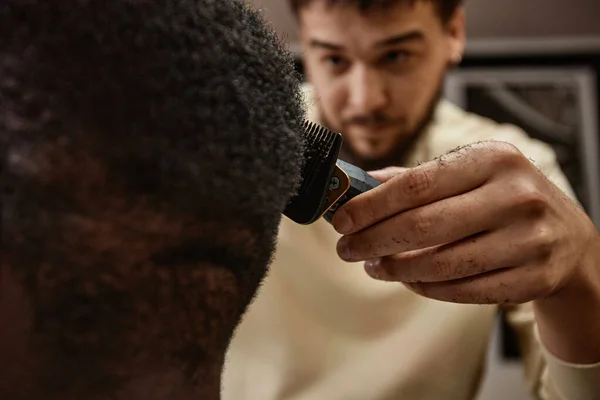 Barber using trimmer to shave the head of customer during his visit to barber shop
