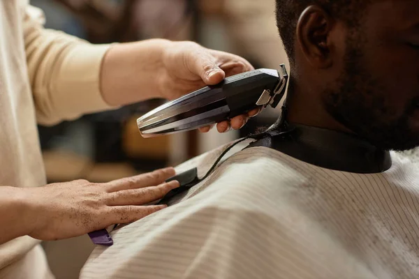 Close-up of hairdresser cutting customer with trimmer in barber shop