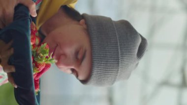 Bir kızın olgun çilek dolu bir konteynırı tutarken ve sera çiftliğinde çalışırken zevkle koklarken dikey pozu.