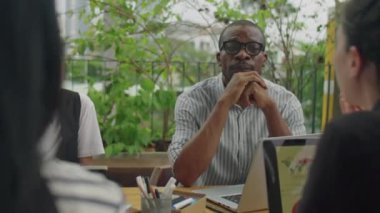 Kafkasyalı genç iş kadını Afro-Amerikalı erkek meslektaşının yanında oturuyor ve açık hava toplantılarında ekiple planlarını tartışıyor.