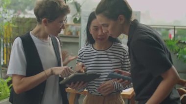 Açık terasta dijital tablette iş projesini tartışan çok ırklı kadın iş arkadaşlarının orta boy görüntüleri.