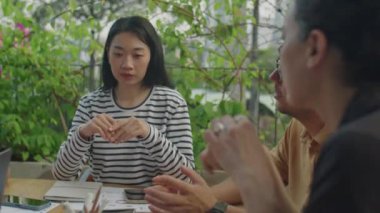 Genç Asyalı kadın açık terasta buluşurken çok ırklı iş arkadaşlarıyla iş görüşlerini paylaşıyor.